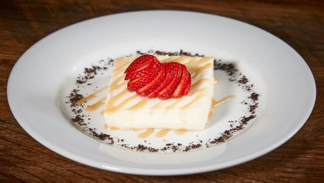 Close-up of cheesecake topped with fresh strawberries and syrup on a white plate.